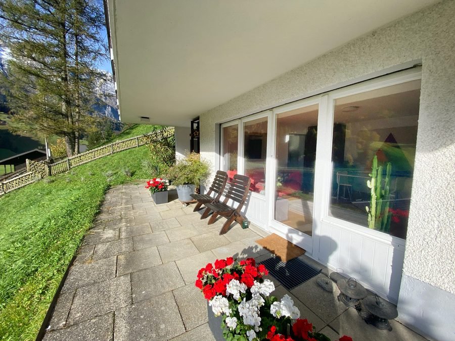Sun terrace with two wooden chairs along the living room windows and the lawn falling away toward the lake