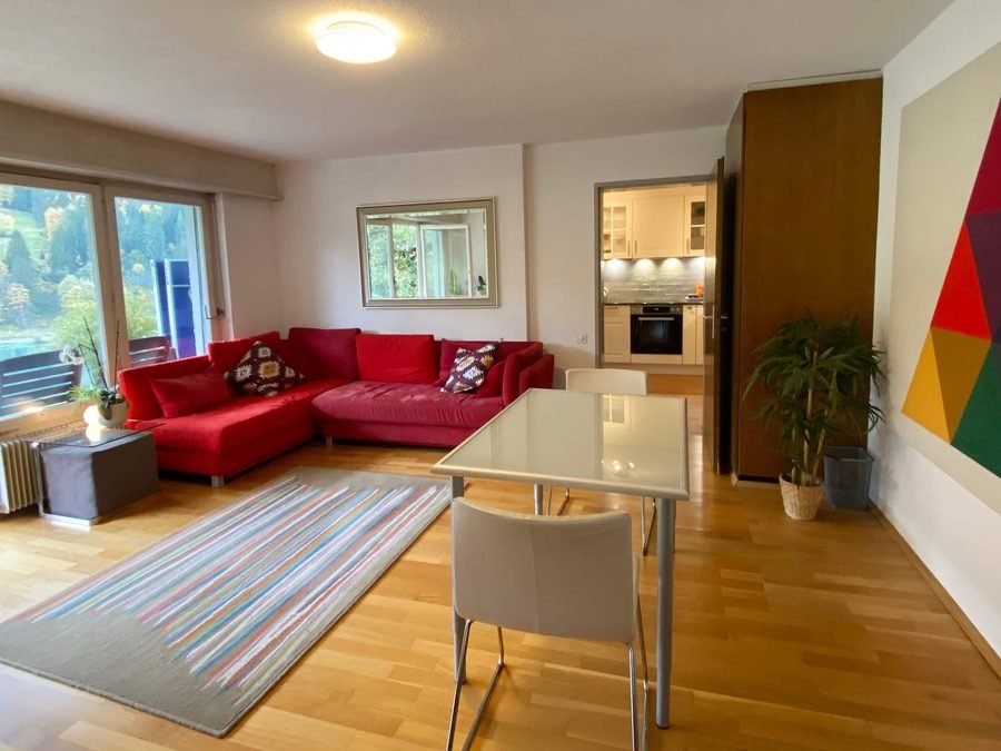 Living room with a red corner sofa, glass dining table and floor-to-ceiling windows onto the terrace