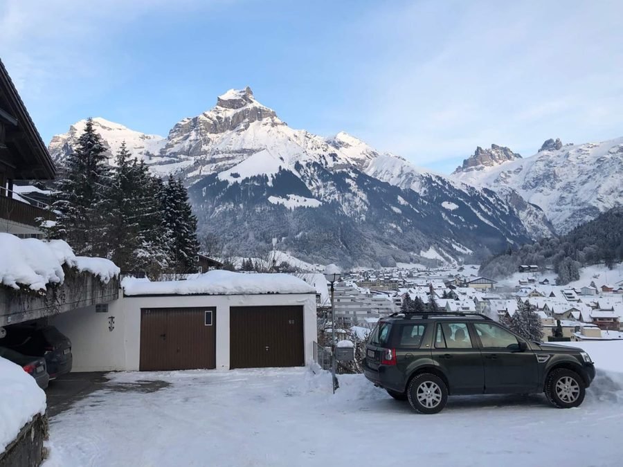 The parking bay above the house in snow, a car parked by the garages, Hahnen and the peaks behind